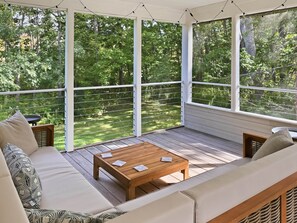 Eine überdachte Terrasse mit Holzboden, einem Holztisch und zwei Sofas mit gemusterten Kissen.