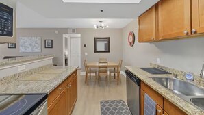 A compact kitchen with granite countertops, wooden cabinets, a dining table with chairs, and a built-in dishwasher.