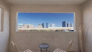 A balcony with a cityscape view, two wooden chairs, and a small round table.