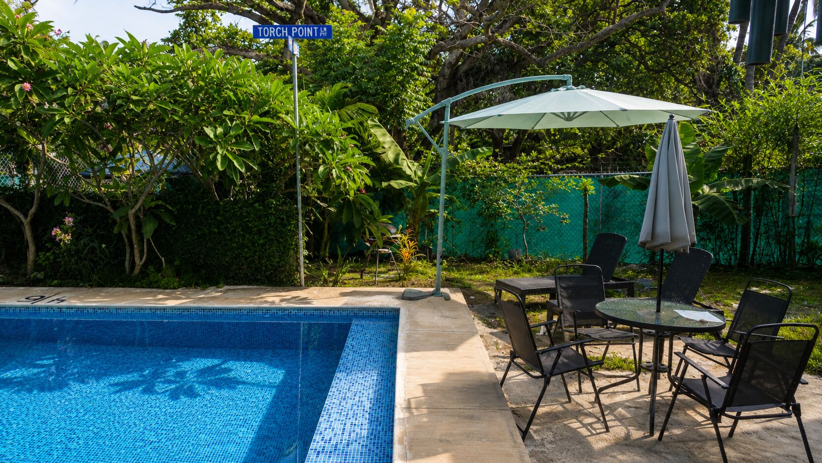 Une piscine dont le bord est revêtu de carrelage, entourée d’une terrasse aménagée avec des meubles d’extérieur et une table couverte.