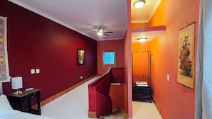 Ein Hotelzimmer mit roter Wand, Deckenventilator, Fenster, Bett, Nachttisch und einem Gemälde.