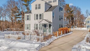 A two-story residential building with a front porch, a driveway, and a snow-covered landscape. - Gorgeous Downtown Townhome - Walk to Beach (Old Orchard Beach)