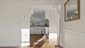 A hallway leading to a kitchen with white cabinets, a wooden floor, and a large mirror on the wall. - Gorgeous Downtown Townhome - Walk to Beach (Old Orchard Beach)
