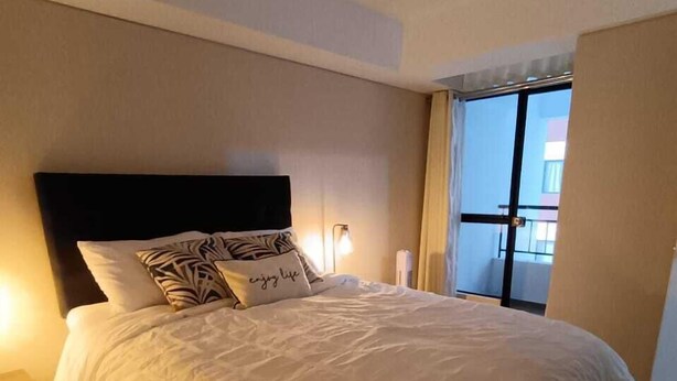 Ein ordentlich bezogenes Bett mit Kopfteil, einer Nachttischlampe und einem Fenster mit Vorhängen.