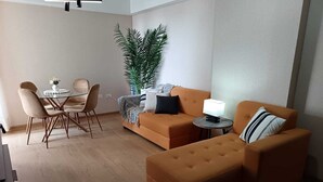 Ein modernes Wohnzimmer mit einer Couch, einem Hocker, einem Couchtisch und einem Esstisch mit Stühlen.