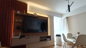 Ein modernes Wohnzimmer mit Fernseher, einem Essbereich mit Stühlen und einem weißen Kühlschrank.