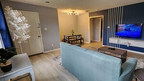 A living room with a blue sofa, a TV mounted on the wall, a small table, and a potted plant. - 2BR Near Sherman College, Wi-Fi + Washer/Dryer (Boiling Springs)