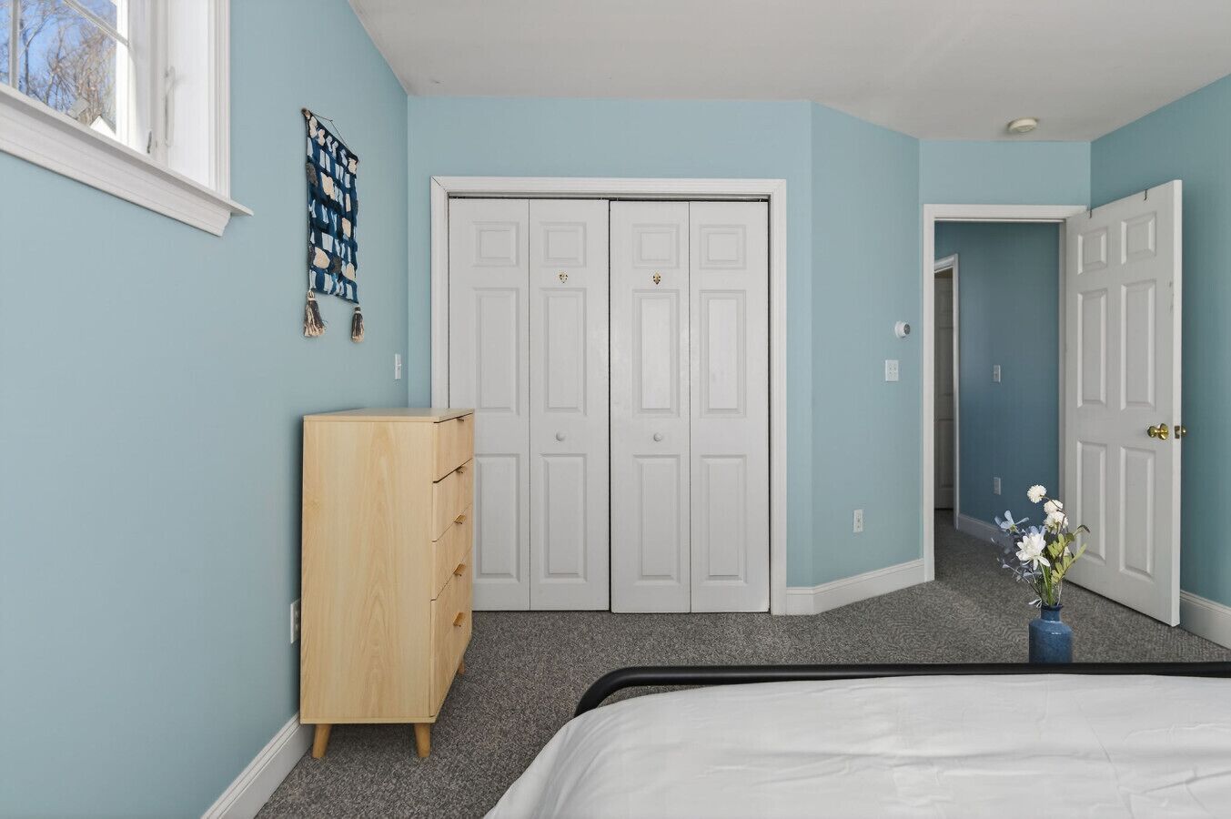 A bedroom with a bed, a dresser, a closet, and a door leading to another room.