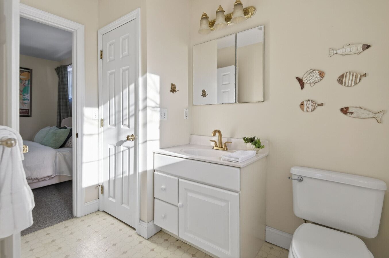 Une salle de bain avec un lavabo blanc, un robinet doré et des toilettes. On y trouve également des décorations murales représentant des poissons et un miroir au-dessus du lavabo.