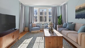Ein Wohnzimmer mit Fernseher, zwei Sofas, einem Couchtisch und einem großen Fenster.