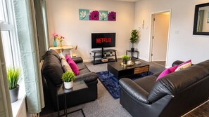 A modern living room with a black leather sofa, a coffee table, and a flat-screen TV mounted on the wall. - Stylish 2-Bed Cardiff Home - Walk to City Centre (Cardiff)
