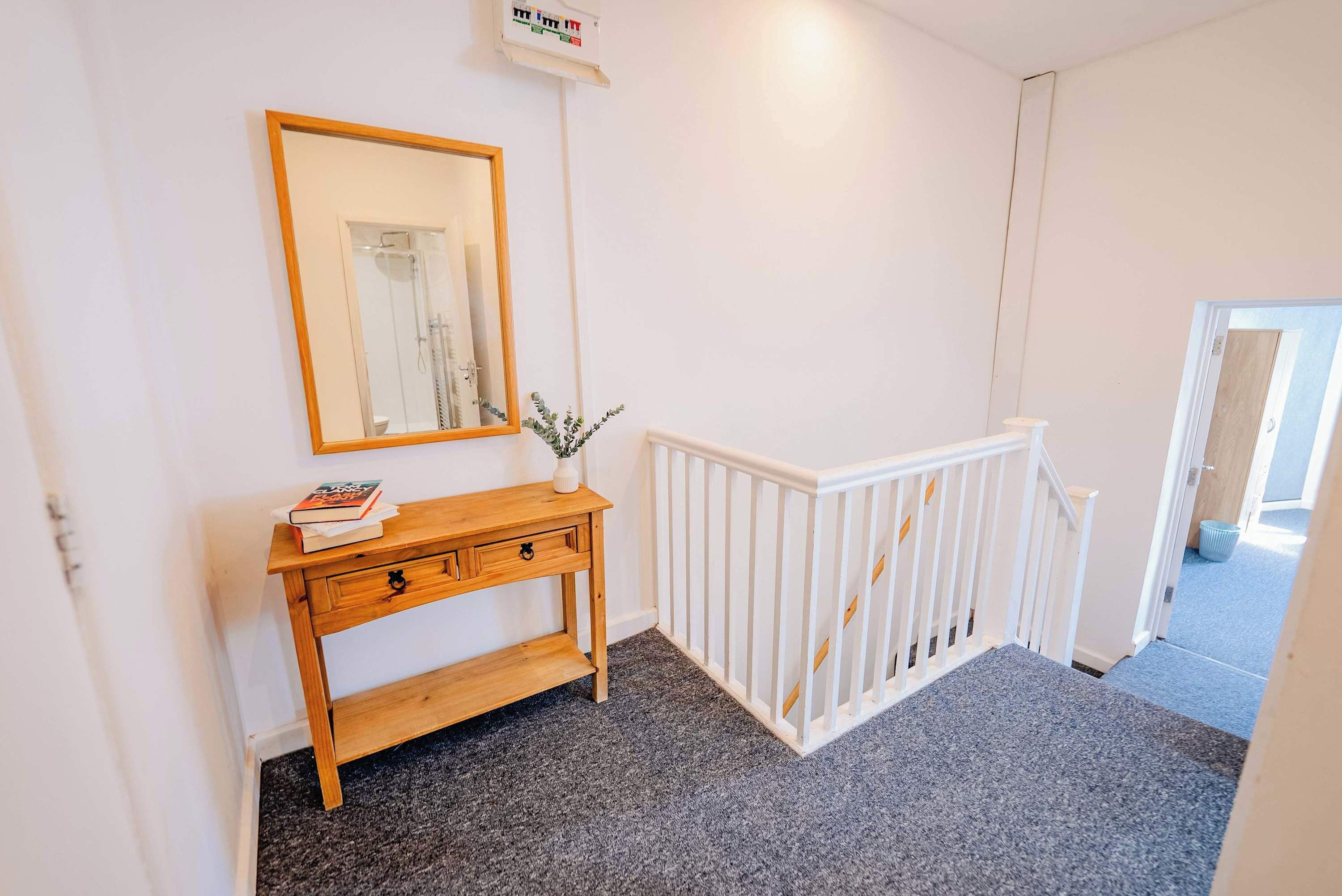 A hallway with a white railing, a wooden console table with a mirror, and a carpeted floor.