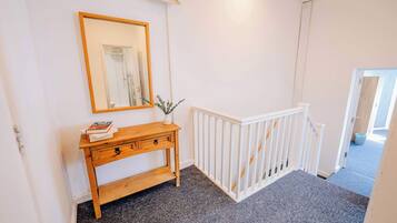 A hallway with a white railing, a wooden console table with a mirror, and a carpeted floor.
