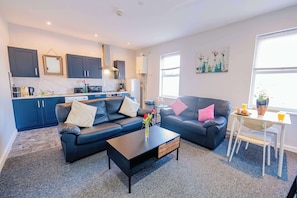 A modern living room with a sofa, coffee table, and a dining area with a table and chairs. - Stylish 2-Bed Cardiff Home - Walk to City Centre (Cardiff)