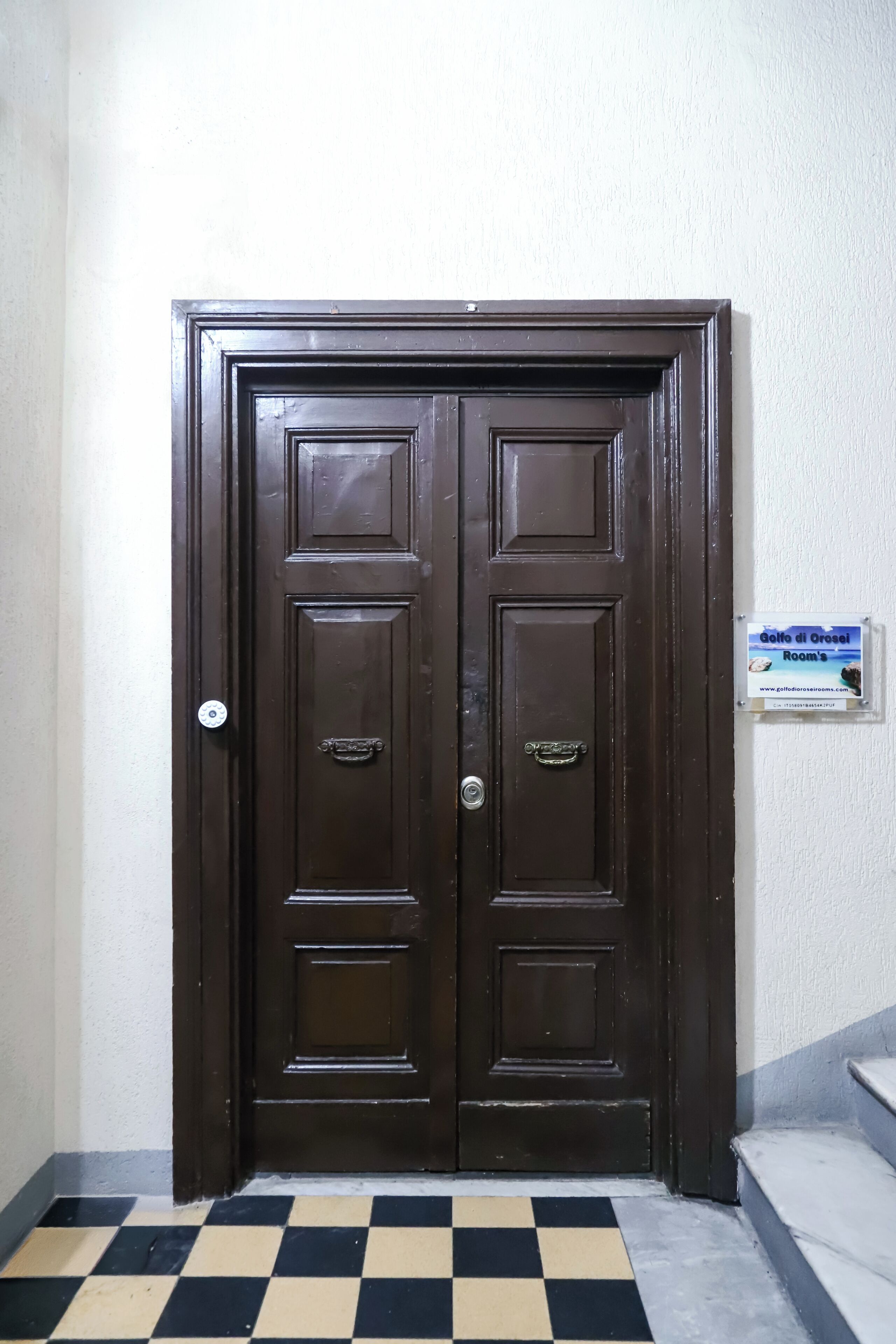 Una puerta doble de color marrón oscuro con un cartel en la pared a la derecha.