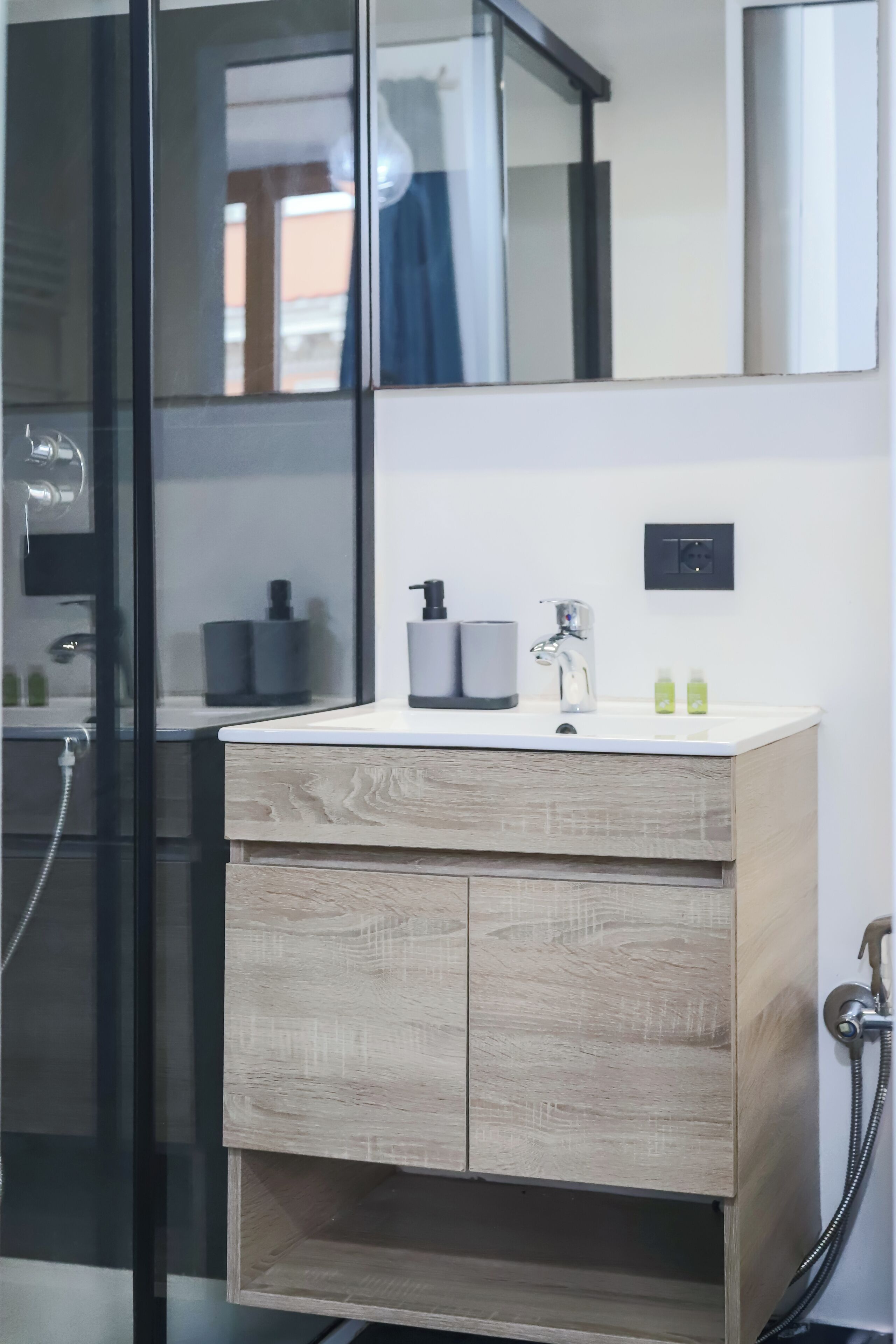 A modern bathroom with a wooden vanity, a large mirror, and a glass shower enclosure.