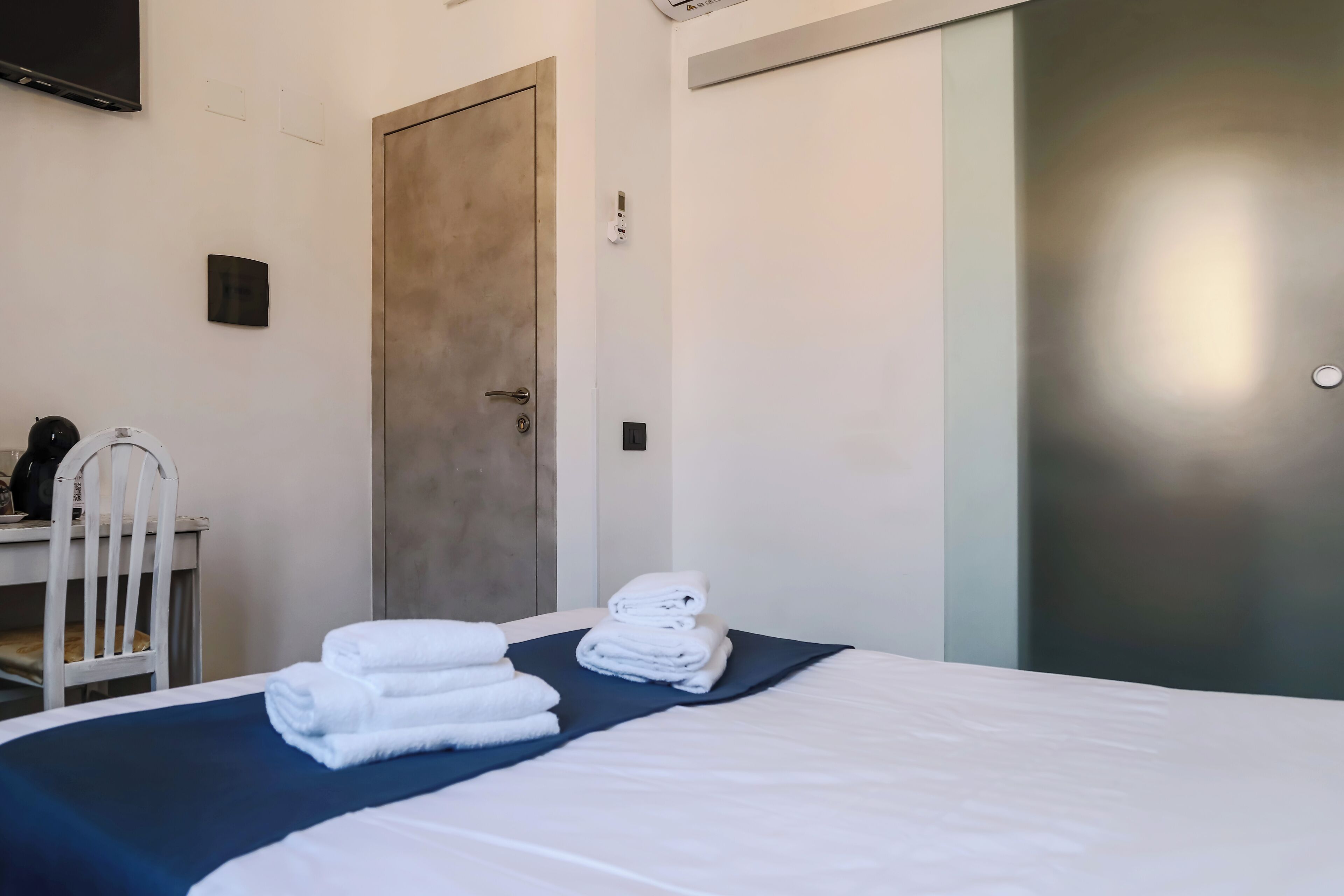 A hotel room with a bed, a desk with a chair, and a door.