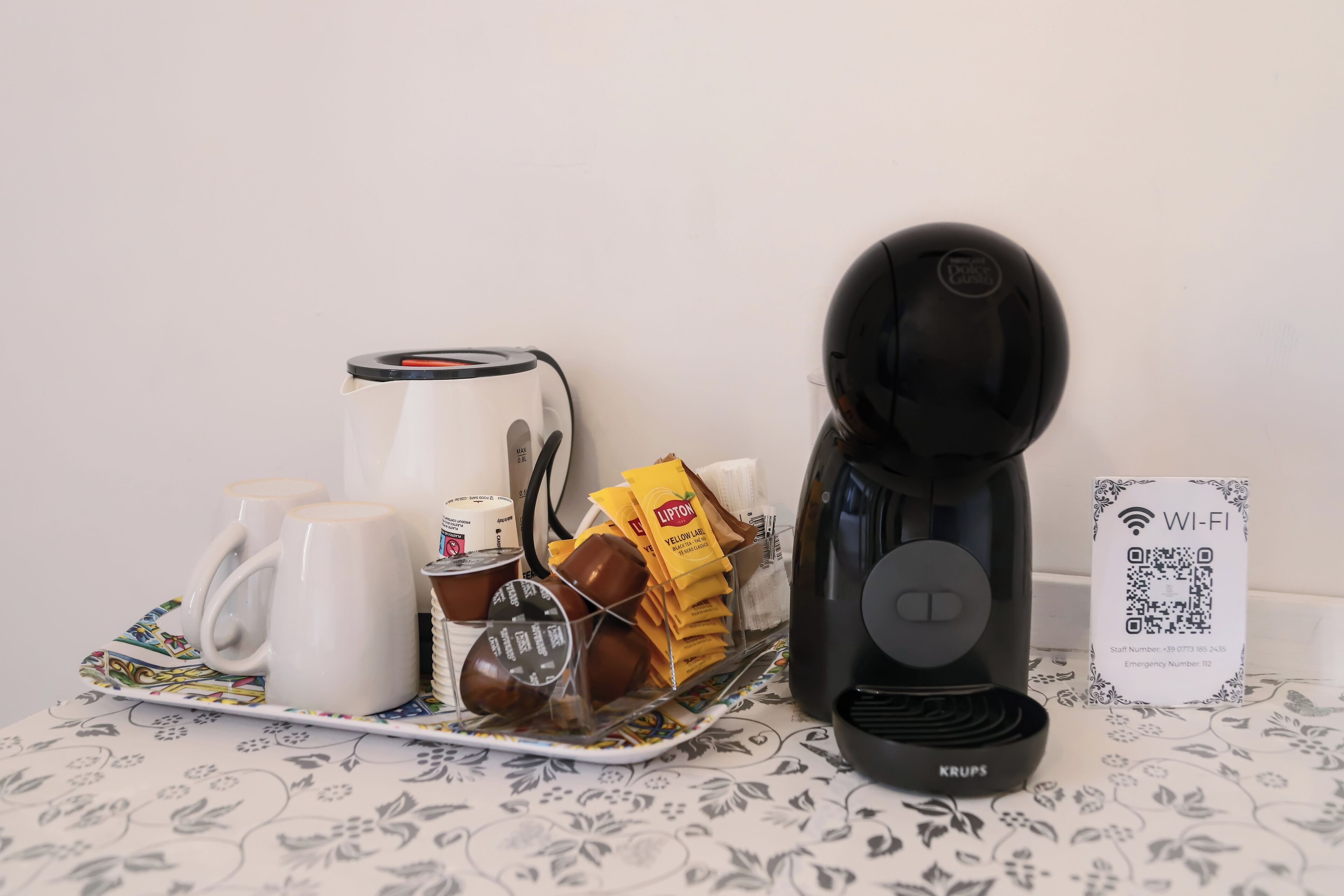 A coffee maker, mugs, a tray with coffee cups and a thermos, a kettle, and a Wi-Fi sign on a table.