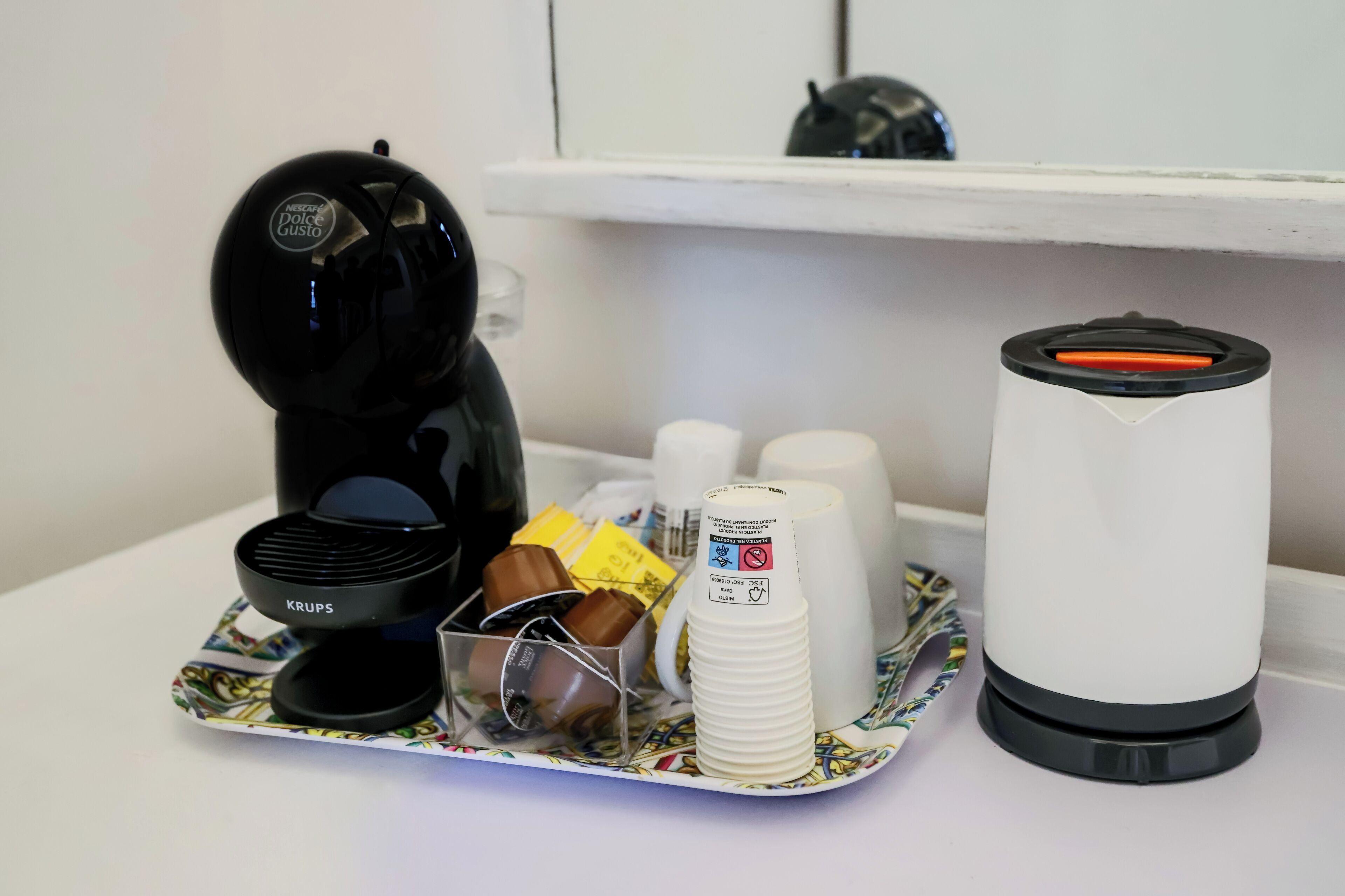 Eine Kaffeemaschine, ein Krups-Kaffeekrug, ein weißer Kaffee-Fontäne und ein Tablett mit Tassen sowie einer Schokoladendose auf einem Tisch.