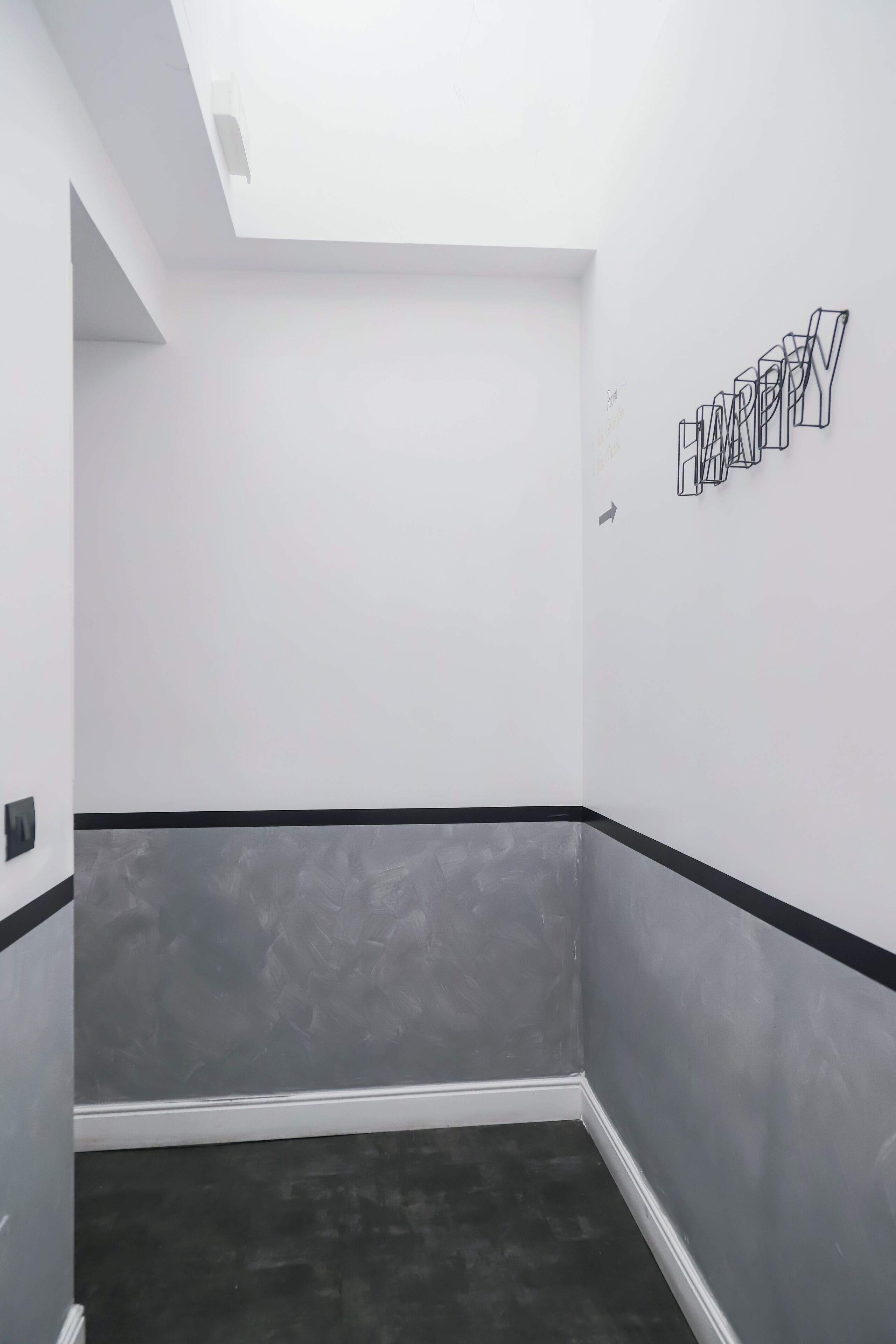 A hallway with a black and white striped wall, a grey textured wall, and a ceiling with a skylight.