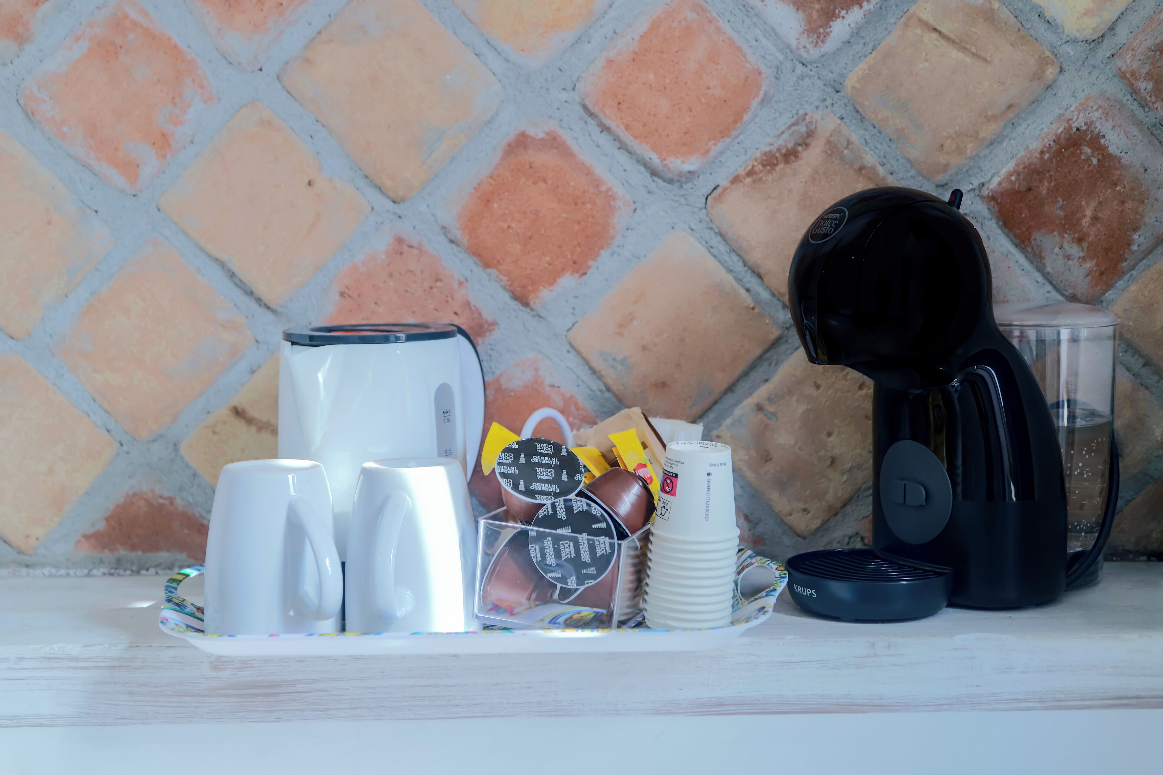 A breakfast setup with a coffee maker, cups, and a tray of food items.
