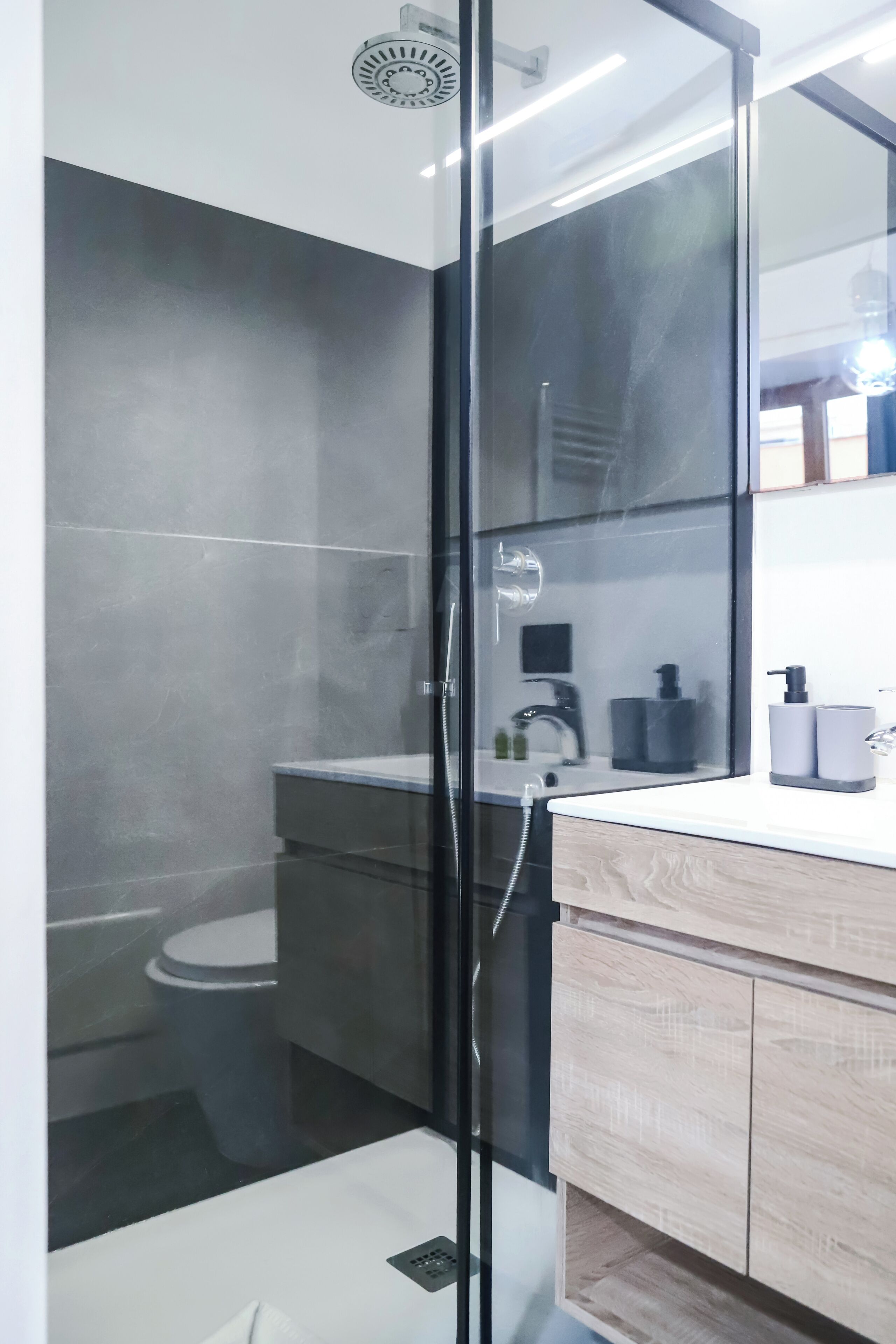 Une salle de bain moderne avec une douche à parois de verre, des toilettes et un meuble-lavabo avec un miroir et des articles de toilette.