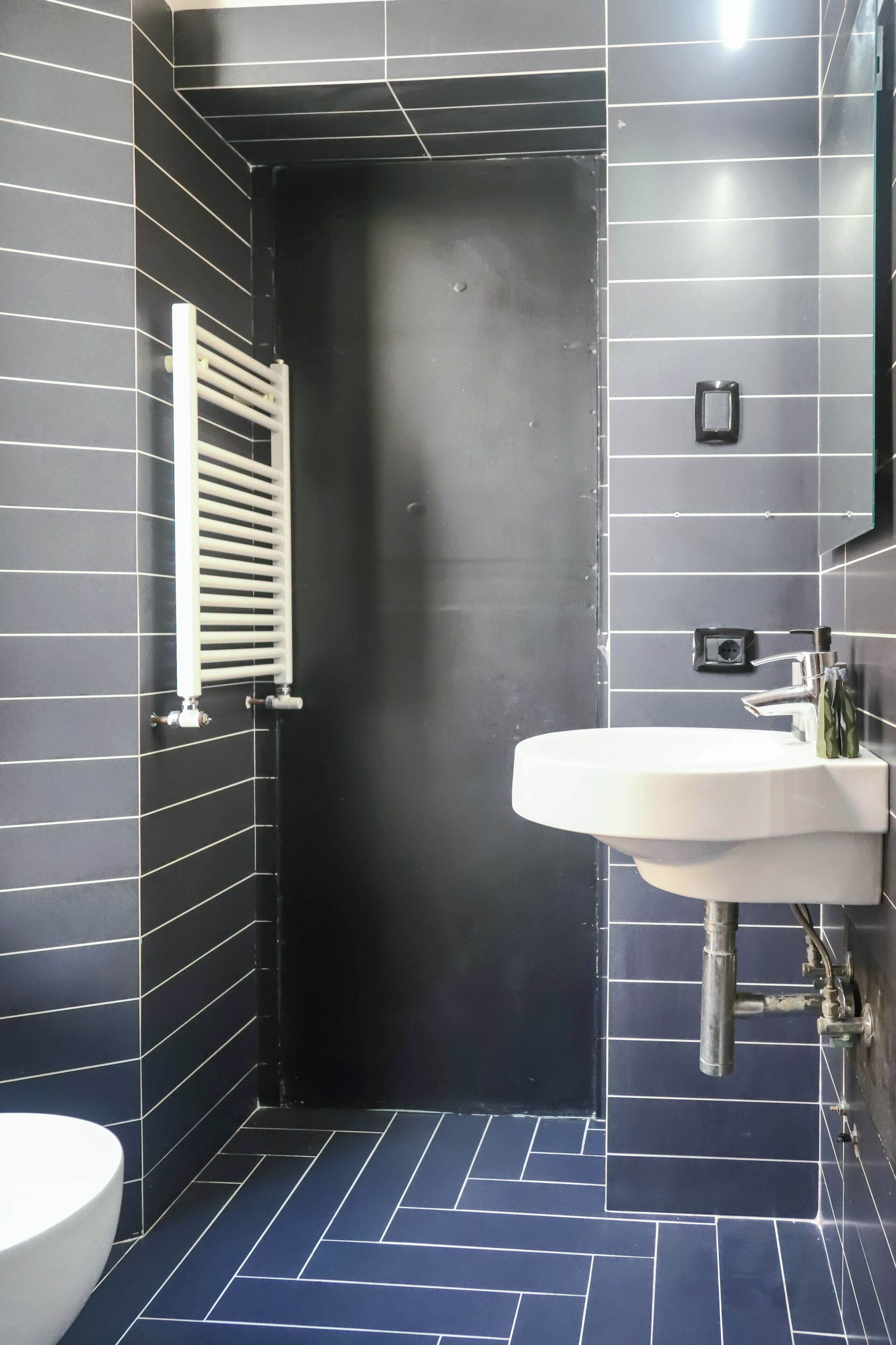 A bathroom with a black door, white radiator, and a white sink.