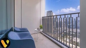 Ein moderner Balkon mit blauen Sitzgelegenheiten, einem kleinen Tisch mit einer Pflanze und Blick auf die Stadt durch ein Metallgeländer.