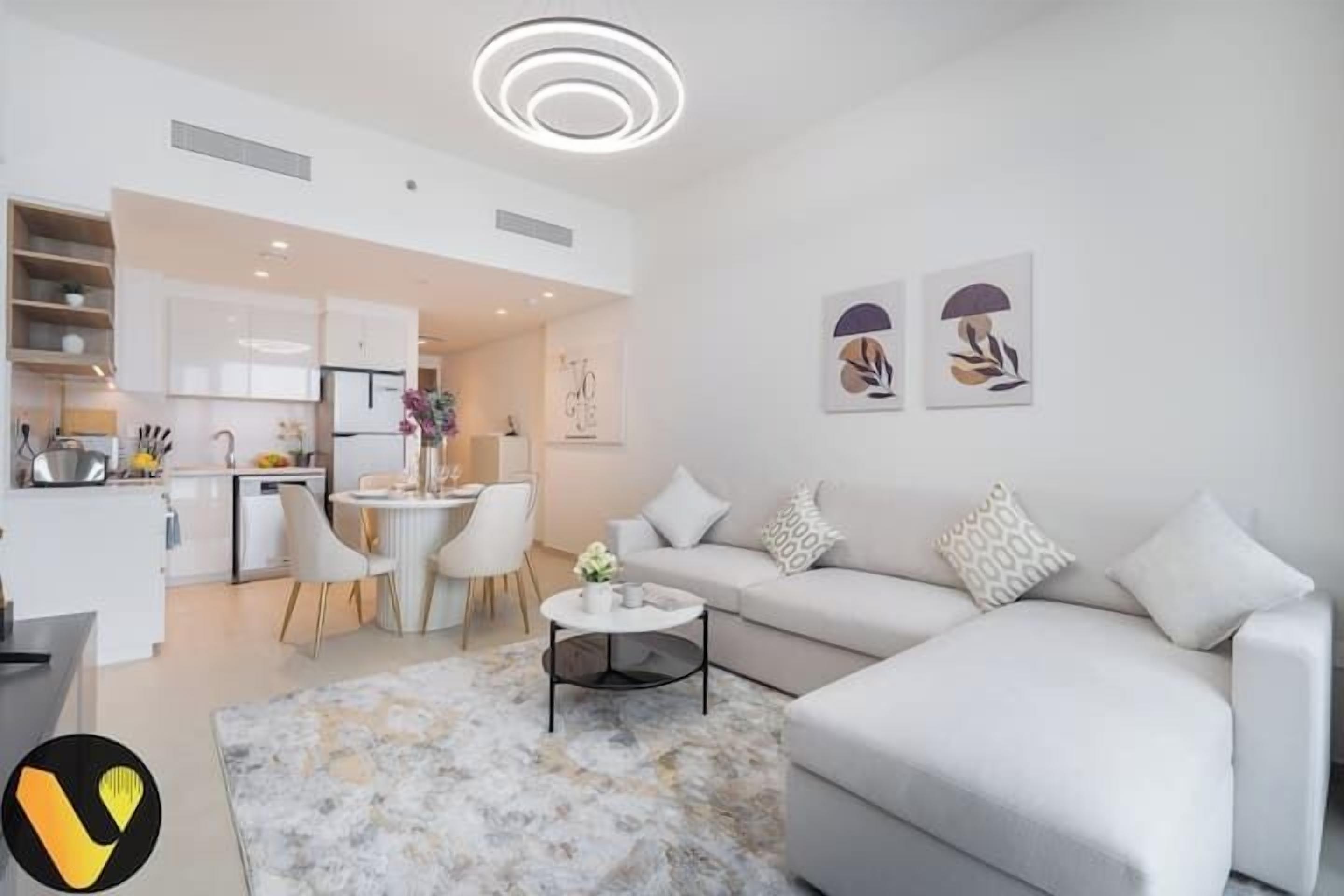 A modern living room with a white sofa, a coffee table, and a dining area with a white table and chairs. There are two framed artworks on the wall.