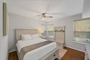Une chambre à coucher comprenant un lit, des tables de chevet, un ventilateur de plafond et une fenêtre avec des stores.