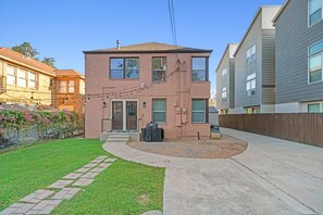 Une maison à deux étages, construite en briques, avec un porche à l’avant, un petit jardin et une allée.