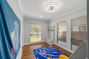 A room with a wooden floor, a ceiling fan, a bench, and a window with blinds.