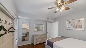 Een slaapkamer met een bed, een kaptafel, plafondventilator en een spiegel.