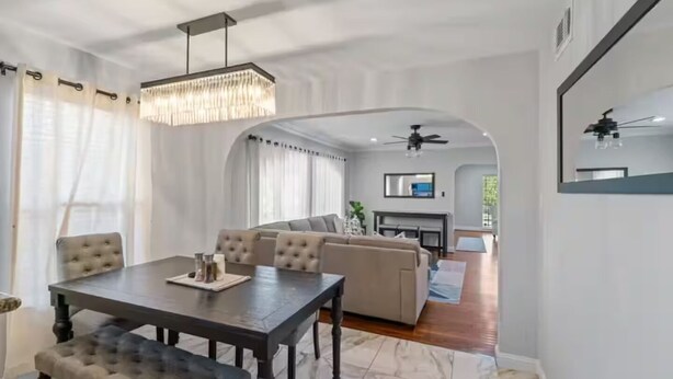 Een moderne woonkamer met een eethoek, met een kroonluchter, een zithoek en een televisie.