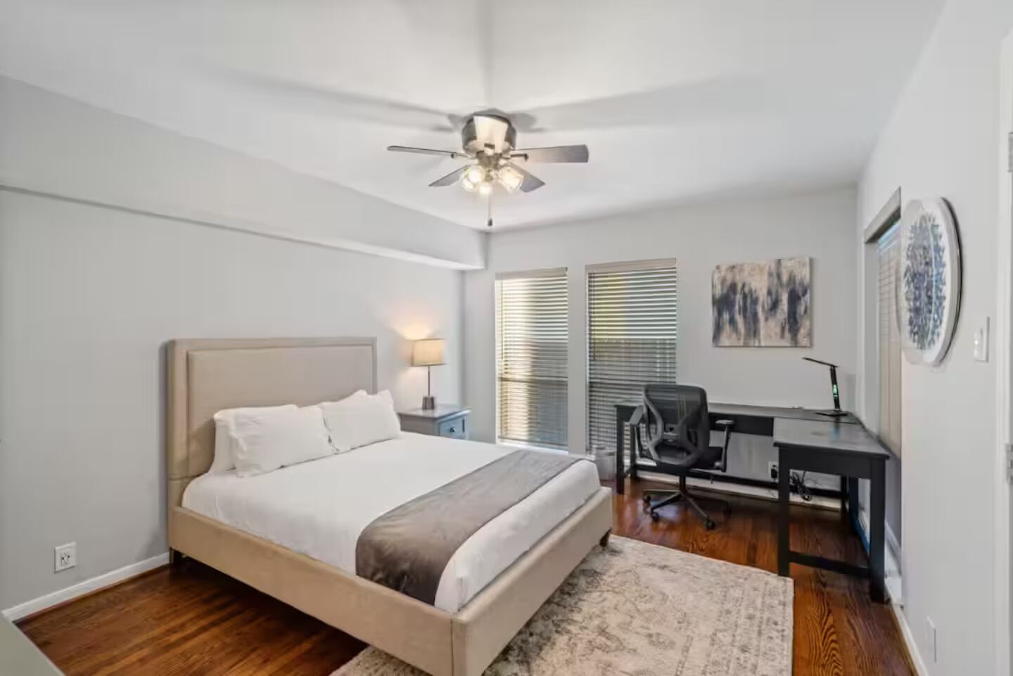 A bedroom with a bed, desk, chair, and ceiling fan.