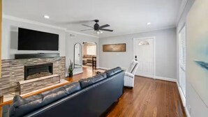 Een moderne woonkamer met een open haard, een zwart leren bank, een flatscreen-tv en een plafondventilator.