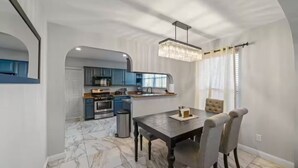 Een moderne keuken met blauwe kastjes, een eettafel met stoelen en een kroonluchter.