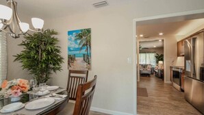 A dining area with a table set for four, a chandelier, a large potted plant, and a painting of a beach scene. - 2 King Beds, Kitchen, Living & Dining Room, Yard, Heated Pool, WiFi, Apt#2112 (Wilton Manors)