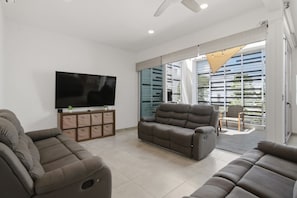 A spacious living room with a large flat-screen TV, two sofas, and a sliding glass door leading to an outdoor area. - Luxury Villa at Bosques De Bambu | Private Pool (Playa del Carmen)