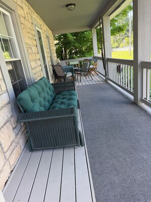 A covered porch with a green sofa, wicker chairs, and a table. - 3-bedroom cottage in Mayville, NY near Chautauqua Institution's Main Gate. (Mayville)