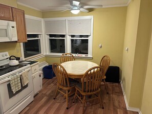 Una cocina con una mesa de comedor, sillas, estufa, microondas y ventilador de techo.