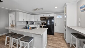 A modern kitchen with white cabinets, a black refrigerator, and a central island with stools. - Cozy Cottage w/ Gorgeous Views - Near the beach! (Galveston)