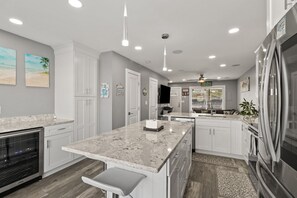 Una cocina moderna con armarios blancos, encimera de granito, electrodomésticos de acero inoxidable e iluminación empotrada en el techo.
