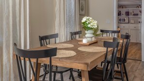 Un coin repas avec une table en bois, des chaises noires et un vase contenant des fleurs blanches.
