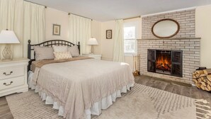Une chambre à coucher avec un lit, des tables de chevet, une cheminée et une fenêtre.