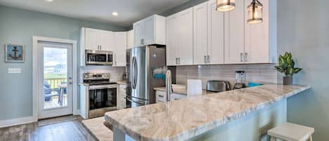 A modern kitchen with white cabinets, stainless steel appliances, and a marble countertop.