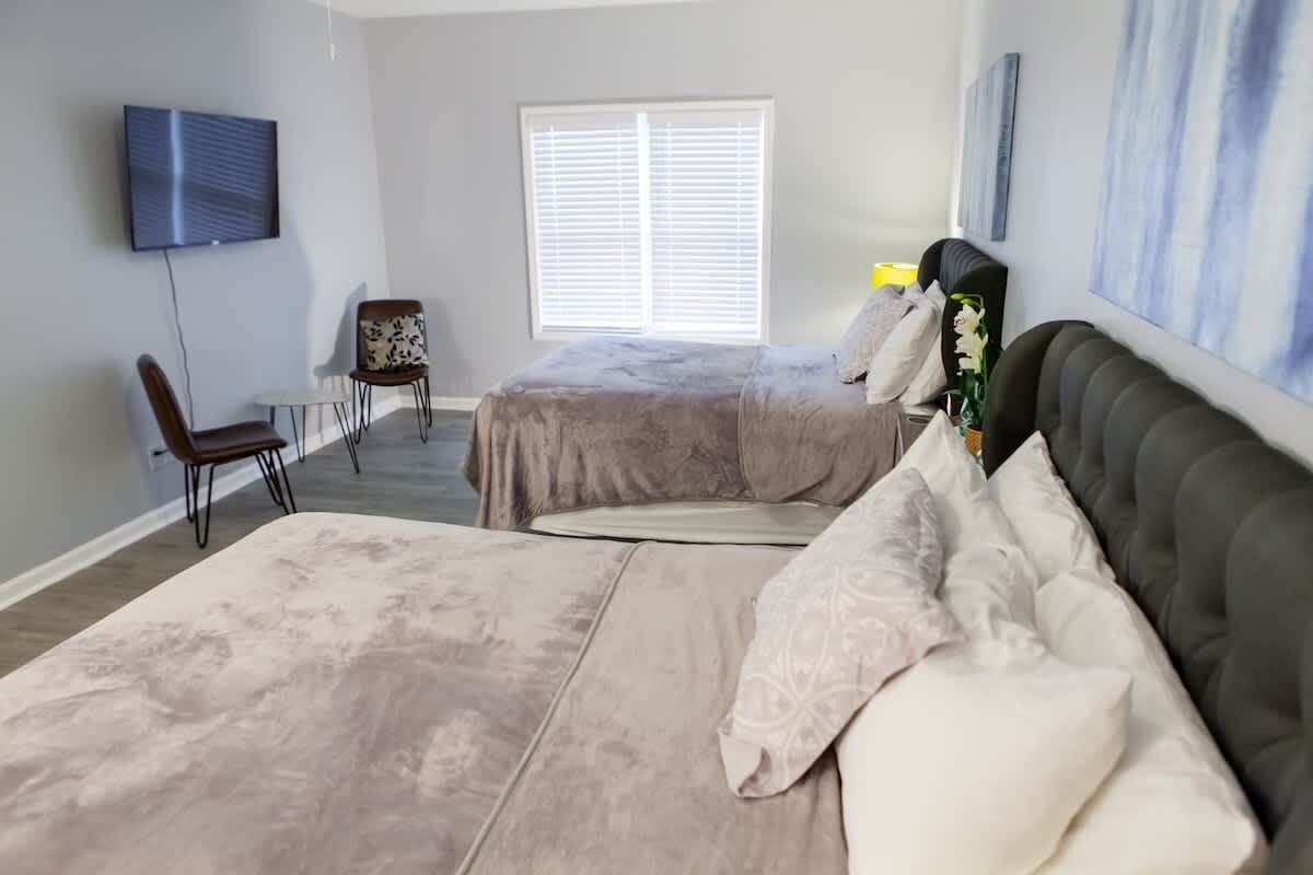 A bedroom with two beds, a TV, a chair, and a window.