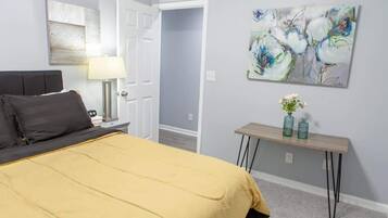 A bedroom with a bed, a nightstand, a lamp, a painting, and a small table with vases.