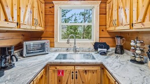 A cabin kitchen with wooden cabinets, a window with a view of trees, a toaster, a coffee maker, and a blender. - Romantic Hot Tub Cabin w/ Fast WiFi | Near Smokies (Sevierville)
