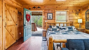 A wooden cabin interior with a bed, a welcome wreath, a framed animal picture, and a wooden door. - Romantic Hot Tub Cabin w/ Fast WiFi | Near Smokies (Sevierville)